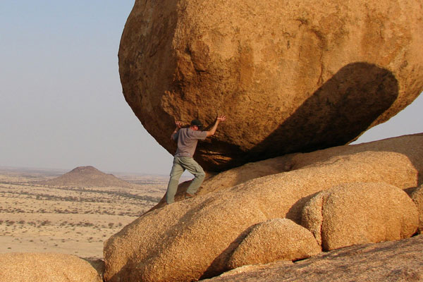A man pushing a giant boulder up a hill